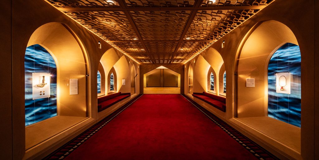 Corredor Omán ONU Nueva York — vista simétrica del pasillo con piezas expuestas en vitrinas y alfombra roja. Producción museográfica de Proasur