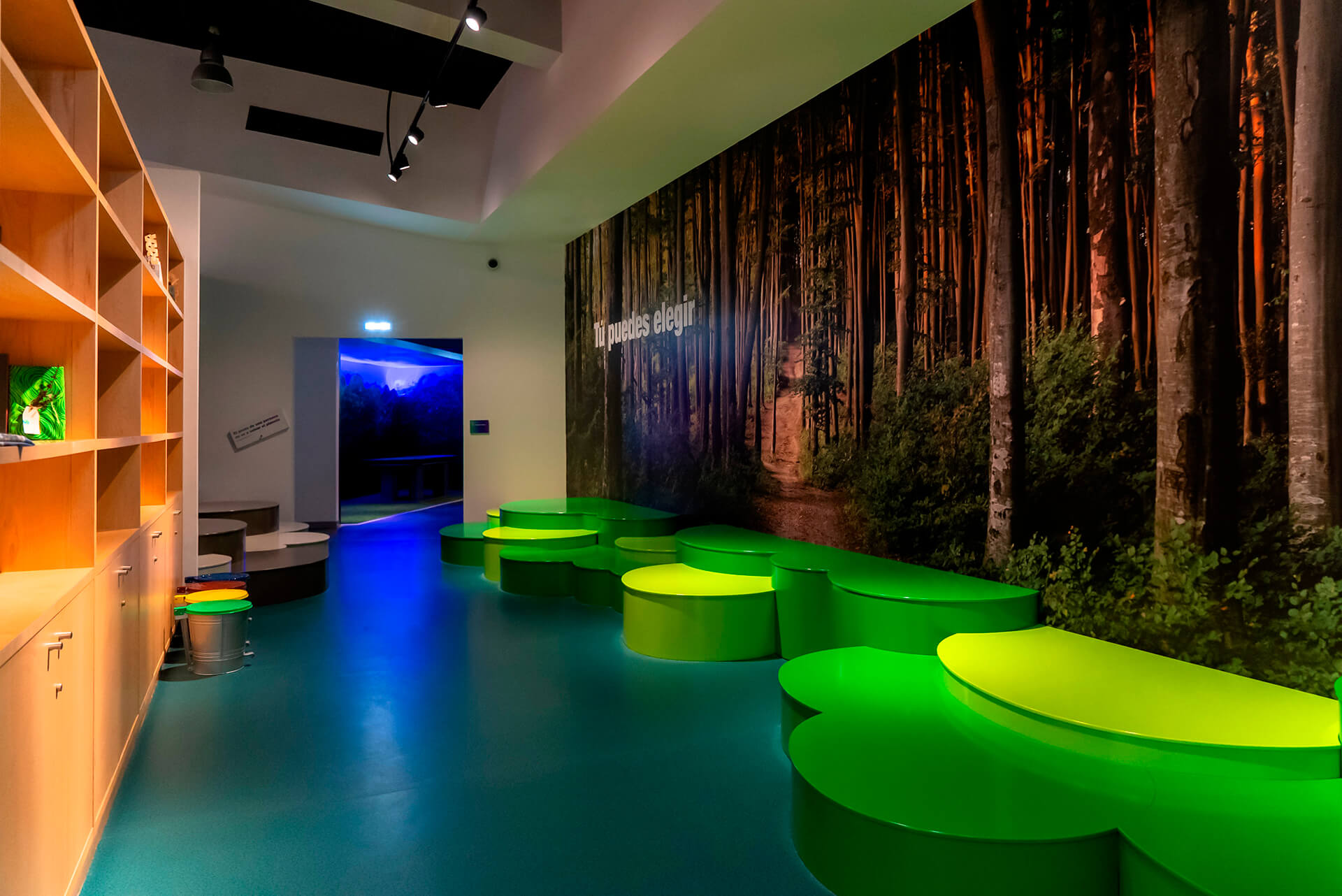 Sala con mural fotográfico de bosque y mobiliario verde en el Centro de Interpretación de Residuos COGERSA